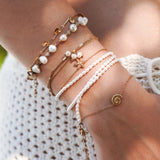 Ensemble de bracelets en acier inoxydable doré, perles, coquillages et étoile de mer sur poignet de femme.