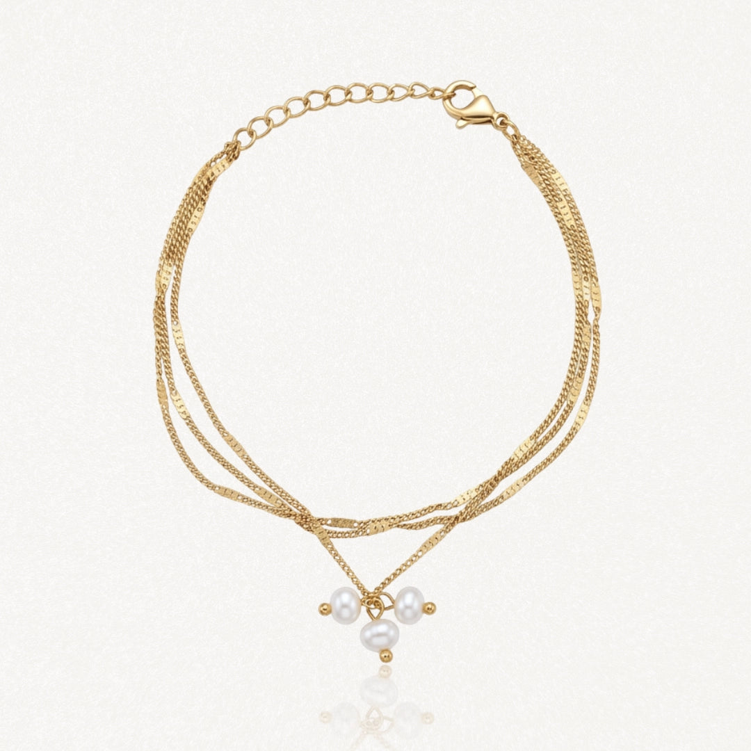 Bracelet doré à trois chaînes fines à maillons plats, fermoir mousqueton, chaînette d'extension et trois perles baroques