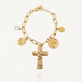 Bracelet MARIE-PIERRE en acier inoxydable doré, composé d'une chaîne à maillons ovales et de quatre pendentifs : une croix texturée, deux médaillons ronds gravés et une petite pierre de zircon transparente en forme de goutte. Le bracelet est posé sur un fond blanc légèrement texturé.