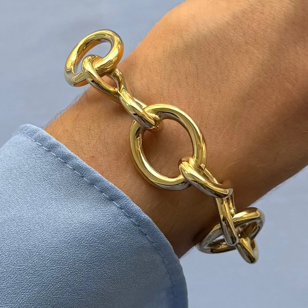 Bracelet jonc maximaliste en acier inoxydable doré en forme de nœud, porté au poignet.