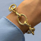 Bracelet jonc maximaliste en acier inoxydable doré en forme de nœud, porté au poignet.