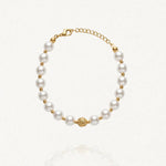 Bracelet MARYLINE composé de perles rondes blanches alternant avec de petites perles dorées, et une perle centrale dorée ornée. Fermoir mousqueton doré.