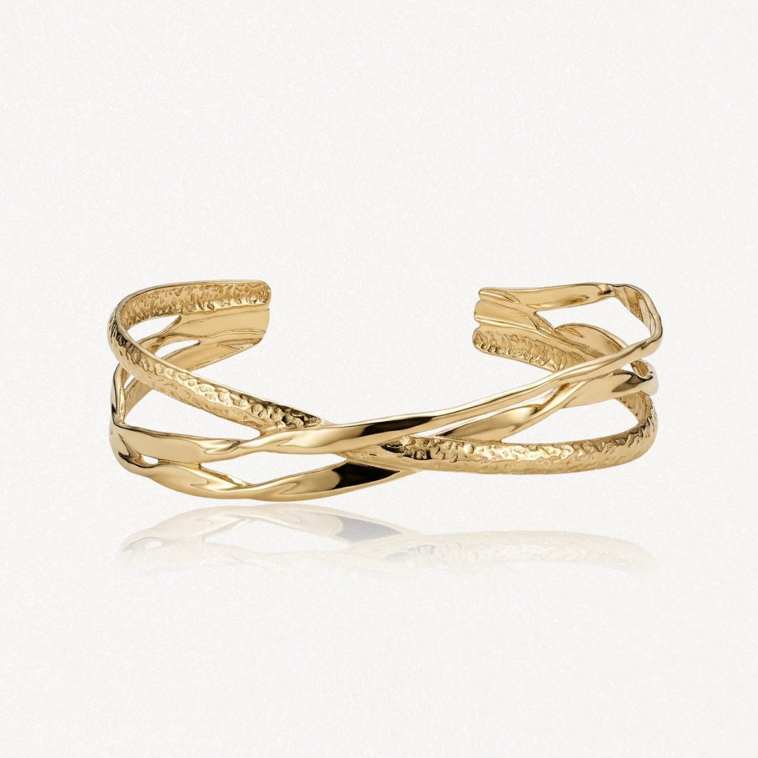 Bracelet manchette doré ouvert, composé de bandes entrelacées lisses et martelées, avec reflets sur fond blanc.