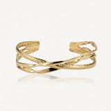 Bracelet manchette doré ouvert, composé de bandes entrelacées lisses et martelées, avec reflets sur fond blanc.