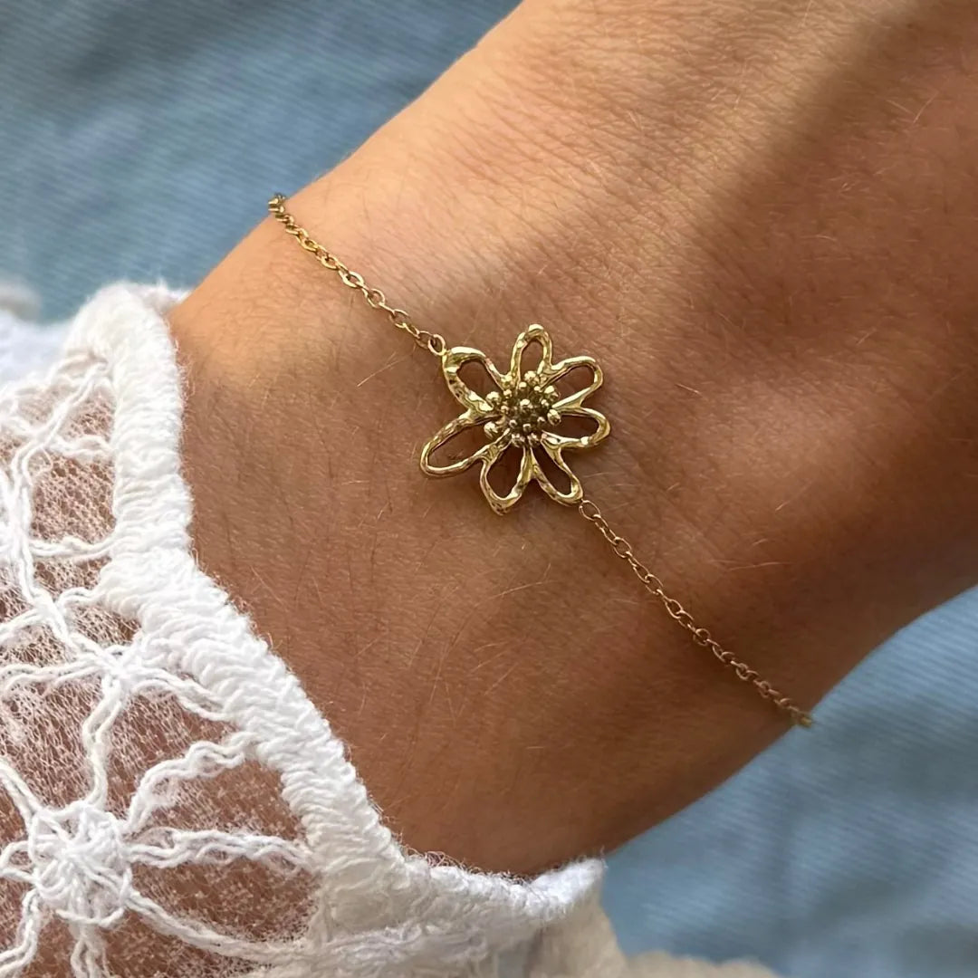 Bracelet fin en acier inoxydable doré avec pendentif fleur ajourée et centre texturé, porté sur un poignet avec une manche en