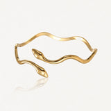 Bracelet doré en forme de serpent ondulé avec deux têtes de serpent se faisant face, chacune ornée d'un petit brillant.