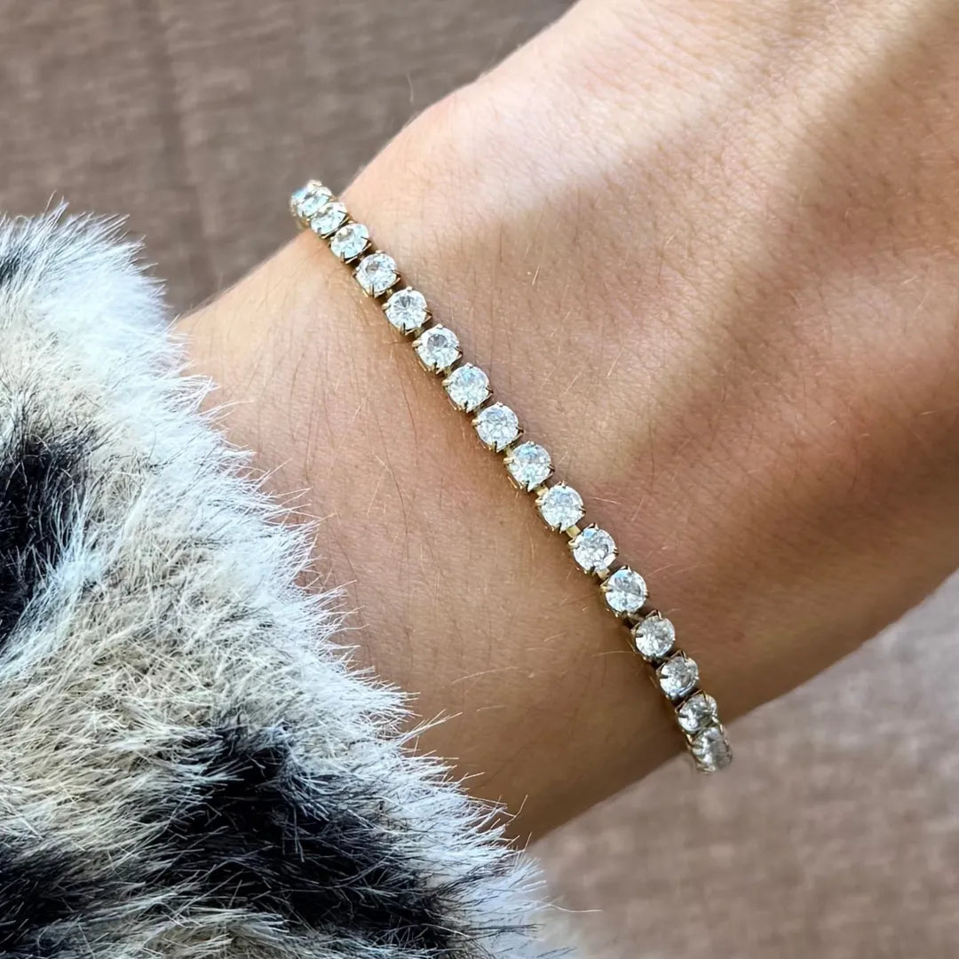 Bracelet tennis en acier inoxydable doré, entièrement serti de zircons blancs, porté sur un poignet et près de fourrure.