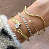 Poignet orné de 4 bracelets en acier inoxydable doré: un tennis serti de zircons blancs, un jonc à gros zircon, un jonc fin