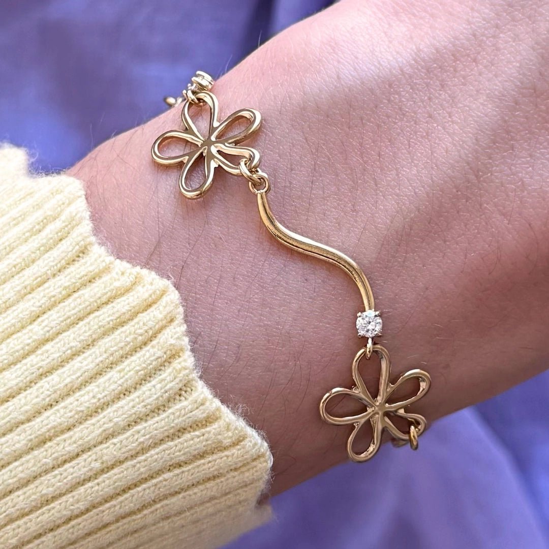 Bracelet en acier inoxydable doré avec maillons fleurs ajourées et zircon central, porté au poignet.