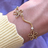 Bracelet en acier inoxydable doré avec maillons fleurs ajourées et zircon central, porté au poignet.