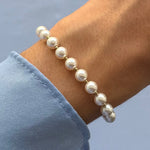 Bracelet perles blanches et billes en acier inoxydable doré porté au poignet, manche de chemise bleue visible.