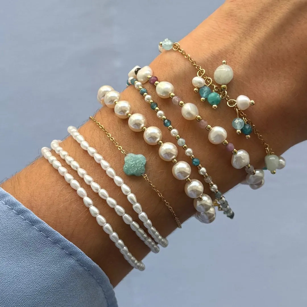 Poignet avec des bracelets en acier inoxydable dore, perles blanches variées, petites pierres naturelles colorées et trèfle