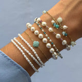 Poignet avec des bracelets en acier inoxydable dore, perles blanches variées, petites pierres naturelles colorées et trèfle