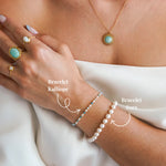 Bracelet Zora de perles blanches en acier inoxydable doré, porté au poignet d'une femme.