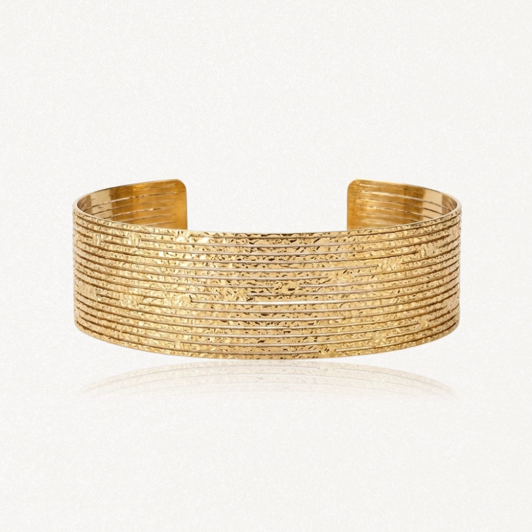 Bracelet manchette large en métal doré, ouvert, avec une surface texturée et de fines bandes horizontales.