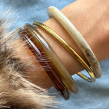 Femme portant une accumulation de quatre bracelets joncs fins en résine naturelle et acier doré au poignet.