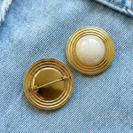 Broche vintage Angela dorée avec cabochon blanc nacré, vue de face et de dos, épinglée sur une toile en jean.