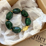 Bracelet vert et or soigneusement emballé dans une boîte d'expédition avec papier de soie, prêt à offrir.