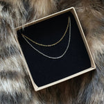 Coffret cadeau MAISON DE L'AMOUR présentant deux chaînes fines minimalistes (coloris or et argent) en acier inoxydable.