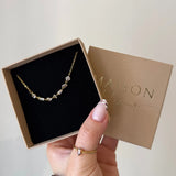 Collier en acier inoxydable doré avec strass en zirconium dans une boîte cadeau tenue par une main