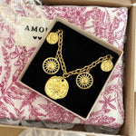 Bracelet chaîne dorée avec 2 charmes soleils, 2 médailles visages, 1 rose des vents, dans sa boîte noire sur tissu toile de Jouy.