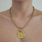 Collier chaîne dorée épaisse à maillons ovales, pendentif médaille irrégulière rose des vents, porté sur cou de femme.