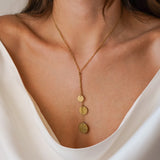 Collier en Y en acier inoxydable doré avec 3 pendentifs ronds martelés, porté sur un décolleté.