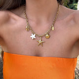 Collier Arya en acier inoxydable doré avec 3 coquillages, une étoile de mer, une feuille et une fleur blanche.