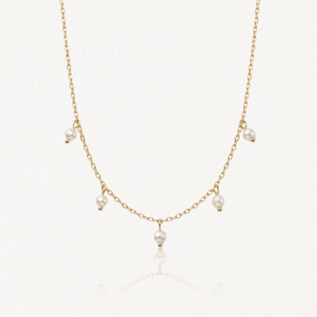 Collier délicat en acier inoxydable doré, chaîne fine avec 5 petites perles blanches pendantes sur fond clair.