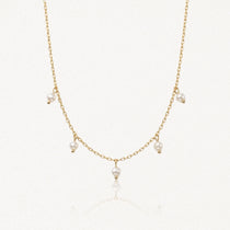 Collier délicat en acier inoxydable doré, chaîne fine avec 5 petites perles blanches pendantes sur fond clair.