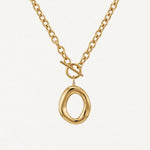 Collier BENEDICTE en acier inoxydable doré. Chaîne à maillons ovales, fermoir toggle et grand pendentif ovale de forme organique irrégulière. Posé sur fond blanc.