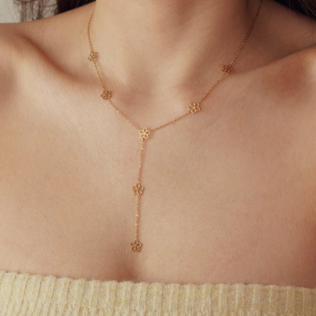 Collier lariat en acier inoxydable doré avec 8 pendentifs fleurs ajourées, porté sur un décolleté féminin.