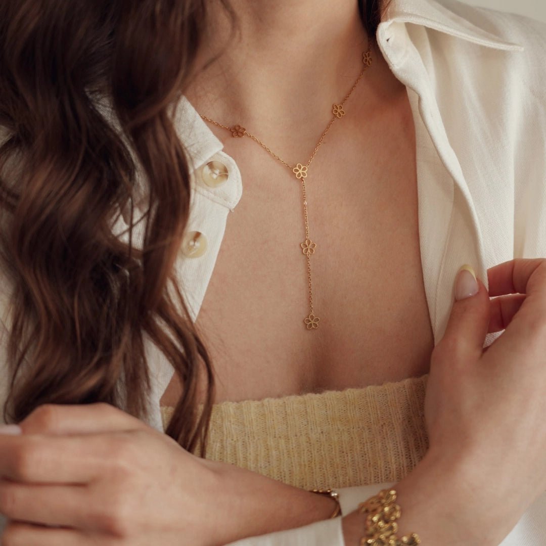 Collier lariat en acier inoxydable doré, motifs fleurs découpées, porté sur le décolleté d'une femme.