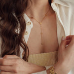 Collier lariat en acier inoxydable doré, motifs fleurs découpées, porté sur le décolleté d'une femme.