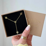 Collier en acier inoxydable doré à motifs fleurs style lariat, dans une boîte cadeau Maison Lamour.