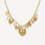 Collier doré MAISON DE L'AMOUR orné de breloques cœurs sacrés ex-voto et de perles blanches sur fond blanc.