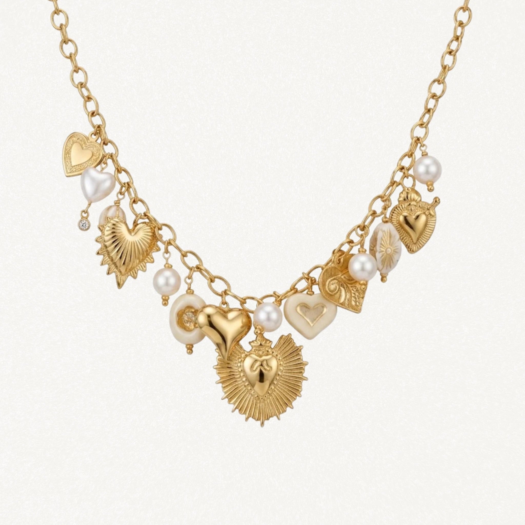 Collier doré MAISON DE L'AMOUR orné de breloques cœurs sacrés ex-voto et de perles blanches sur fond blanc.