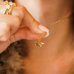 Collier pendentif chien teckel en acier inoxydable doré, tenu par une main. La chaîne est fine.