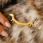 Broche chien teckel en acier inoxydable doré, avec épingle à nourrice visible, sur fourrure. Une main aux ongles clairs