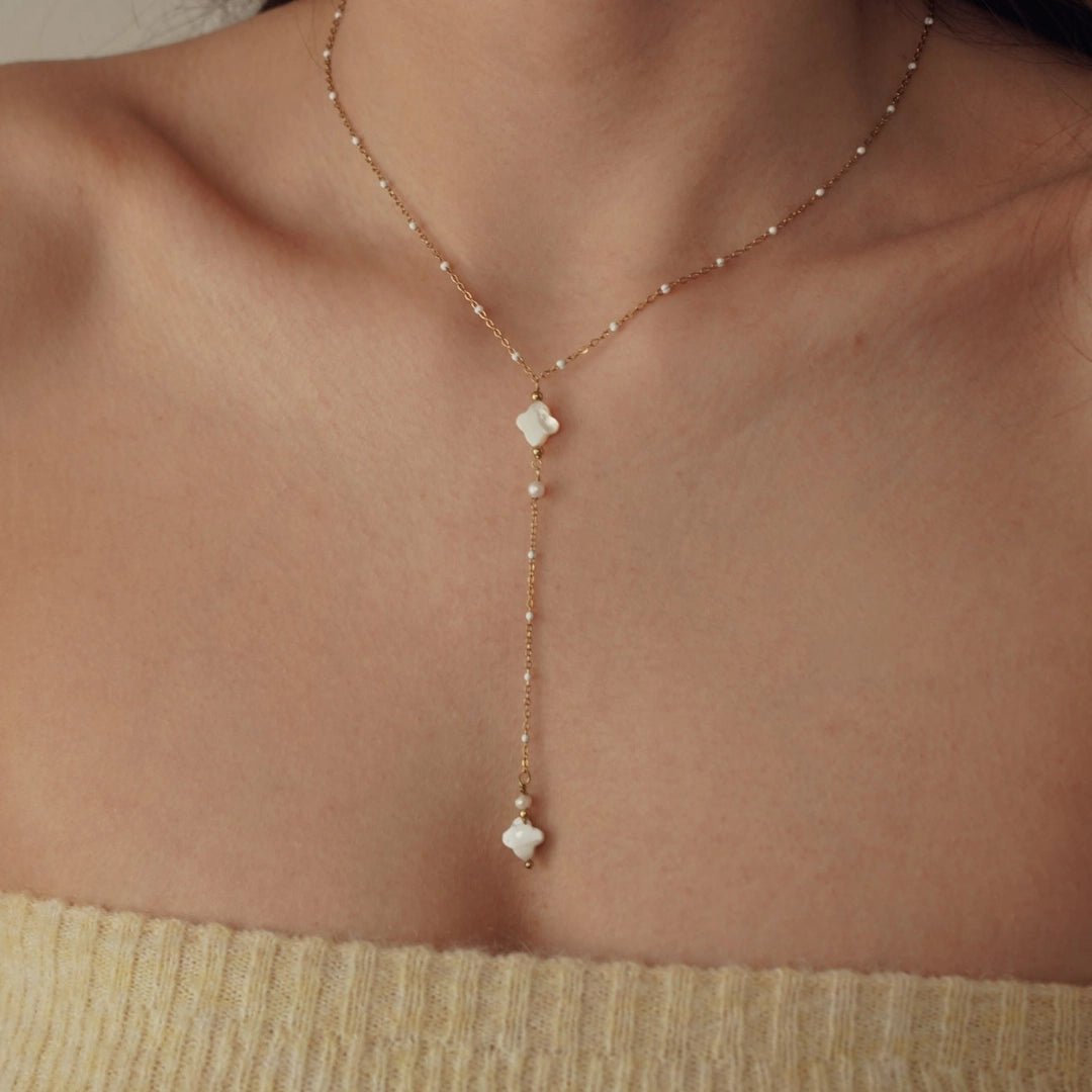 Collier Y en acier inoxydable doré, chaîne fine avec perles blanches, pendentifs trèfles en nacre sur décolleté.