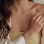 Collier en acier inoxydable doré style Y avec perles et pendentifs trèfles blancs en nacre porté par une femme.