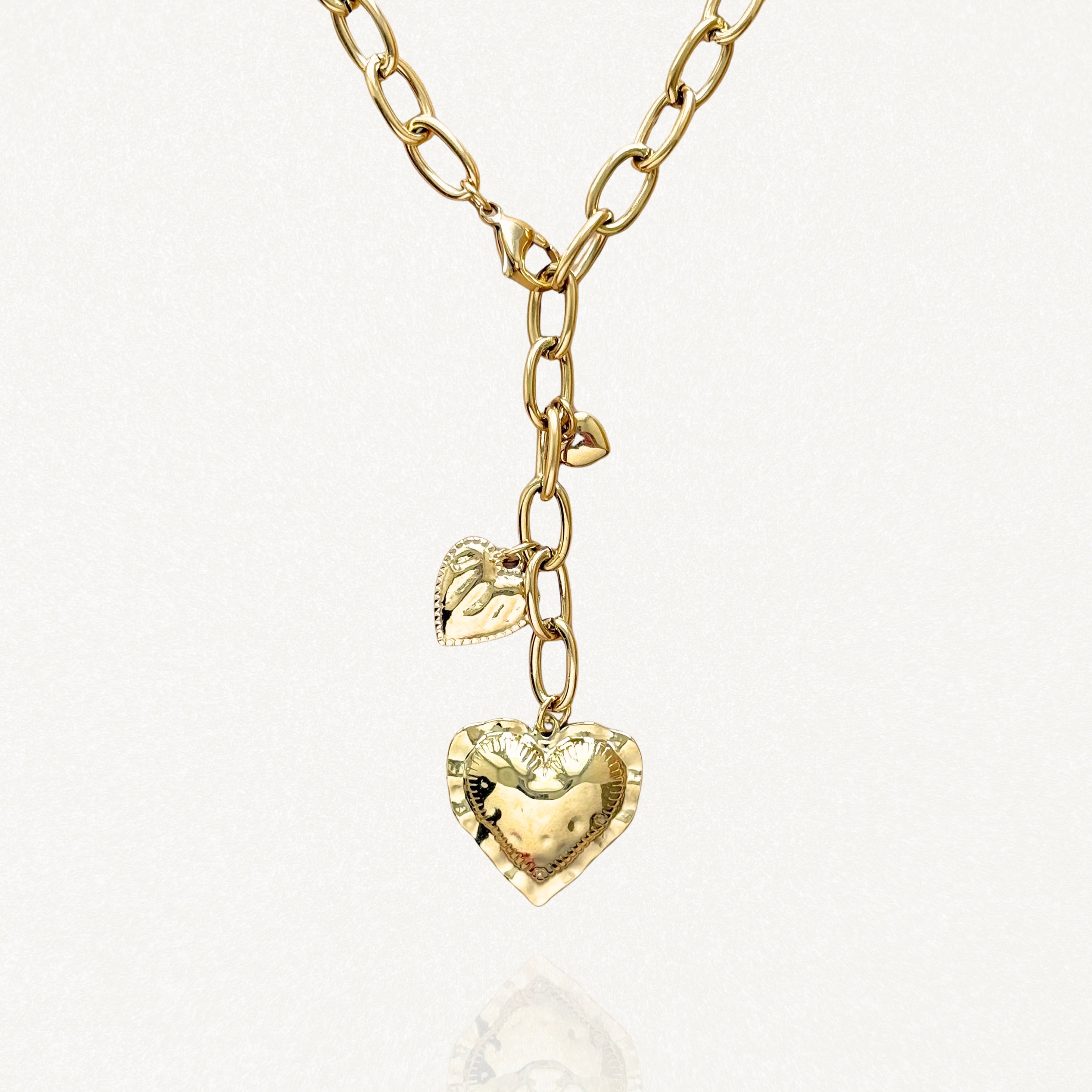 Collier forme Y MAISON DE L'AMOUR en acier inoxydable doré, chaîne à gros maillons et pendentifs cœurs effet martelé sur fond blanc.