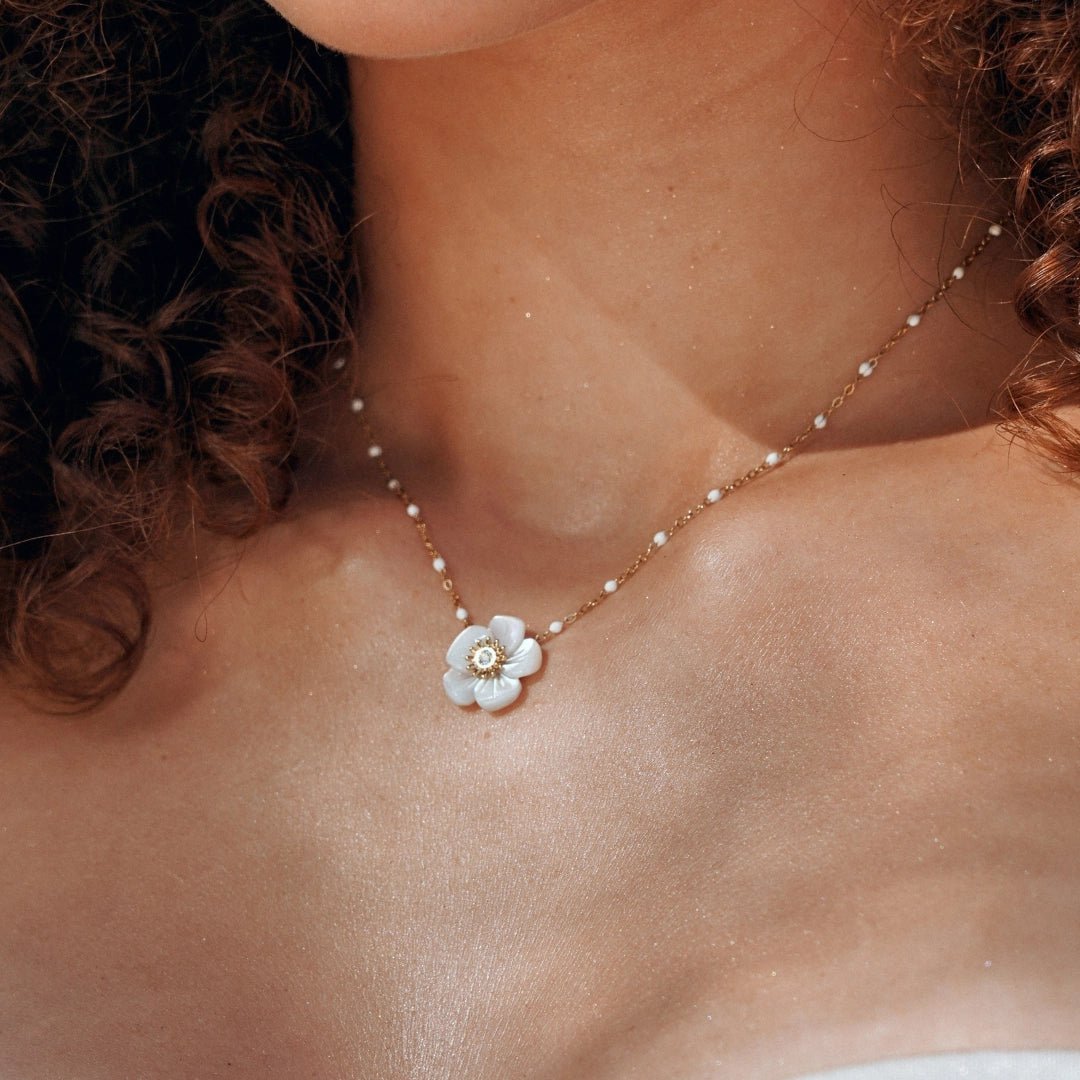 Collier en acier inoxydable doré, chaîne perlée blanche, pendentif fleur blanche en nacre avec zircon, porté par une femme.