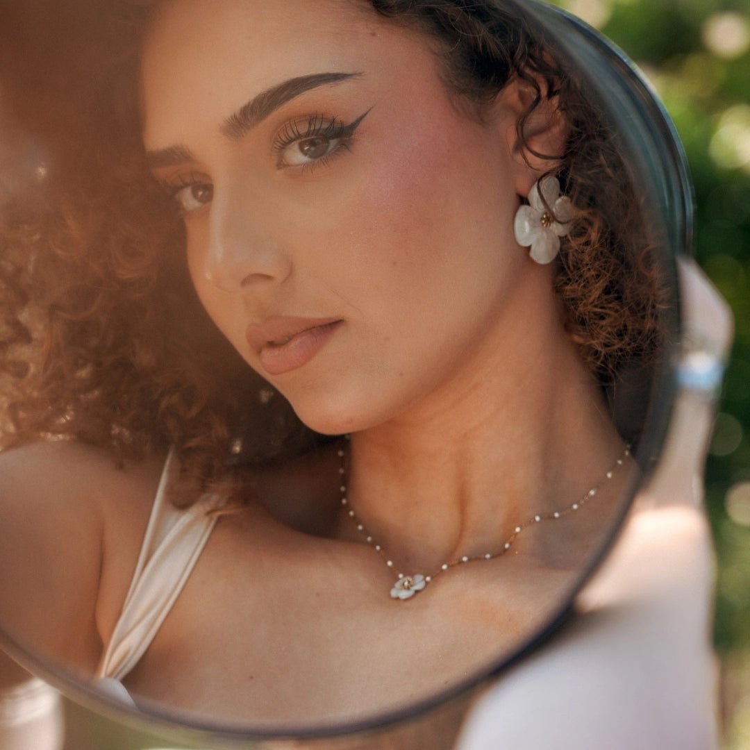Image d'un collier en acier inoxydable à pendentif fleur blanche et petites perles, porté par une femme se regardant dans un