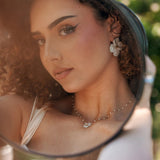 Image d'un collier en acier inoxydable à pendentif fleur blanche et petites perles, porté par une femme se regardant dans un