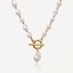 Collier en acier inoxydable doré avec perles baroques blanches, fermoir toggle et perle pendante.