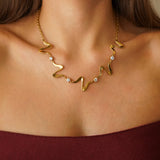 Collier ondulé en acier inoxydable doré et petits zircons brillants, porté sur un décolleté féminin.