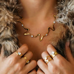 Collier statement ondulé en acier inoxydable doré et 5 zircons. Porté par une femme sur un vêtement en fourrure.