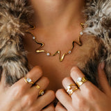 Collier statement ondulé en acier inoxydable doré et 5 zircons. Porté par une femme sur un vêtement en fourrure.