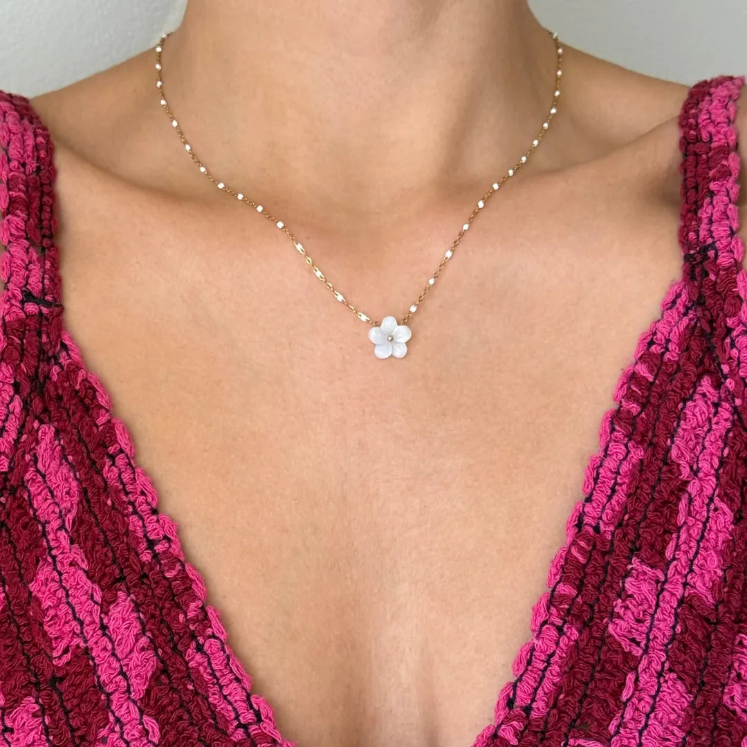 Collier en acier inoxydable doré maille perlée avec pendentif fleur en nacre, porté sur le décolleté d'une personne en haut